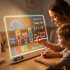 A young girl and boy draw on a glowing LED drawing board featuring colorful rainbows, suns, and math equations.