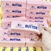 A collection of pink butter stick fidget toys in various sizes and packaging are shown being held by a hand.