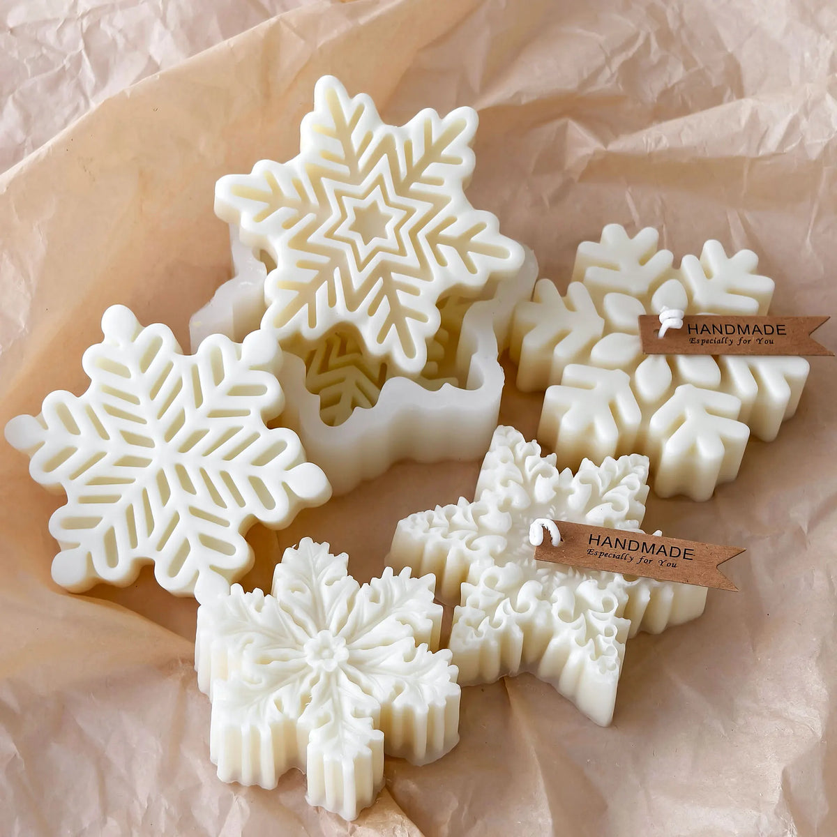 White snowflake silicone molds for candle, soap, and wax melts displayed on brown paper.