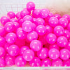 A large quantity of bright pink and purple plastic play balls are displayed in a white basket.