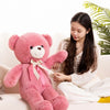 A young woman is sitting on a couch holding a large pink teddy bear plush toy.