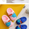 A set of pink and blue cartoon dinosaur plush slippers shown on a yellow surface.