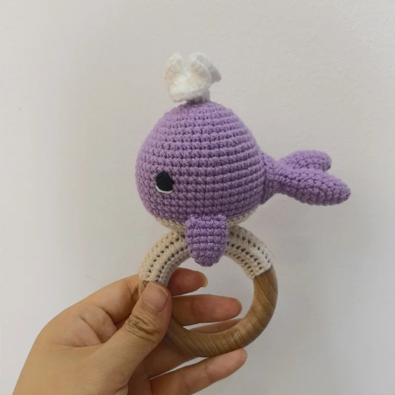 A purple knitted otter rattle and teether ring made of wood is held in a hand.