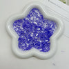 A white flower-shaped dish filled with purple iridescent acrylic ice strips for nail art and DIY crafts