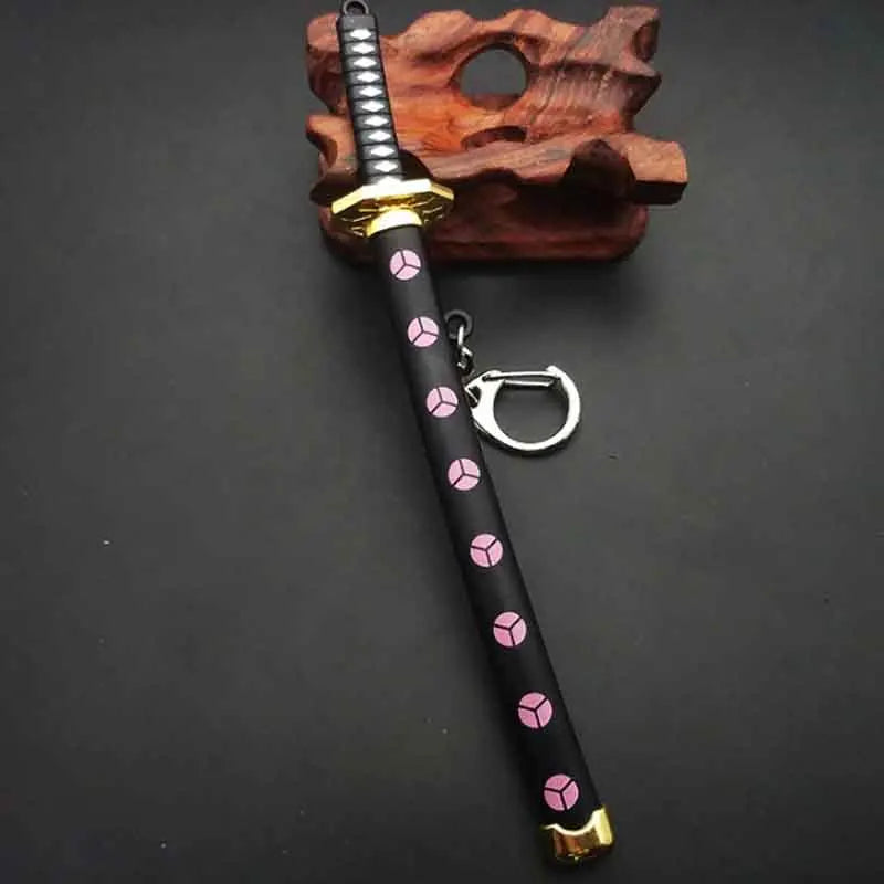 A samurai sword keychain with a black handle decorated with pink cubes and a gold hilt, resting on a wooden block.