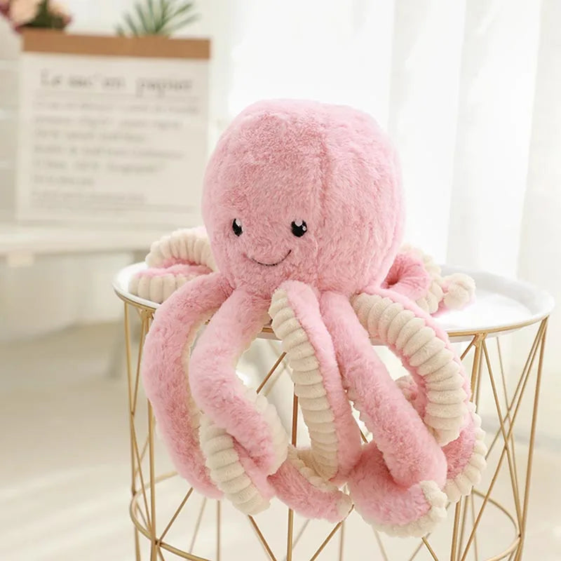 A pink and cream plush octopus toy with hanging loops displayed on a gold wire stand.