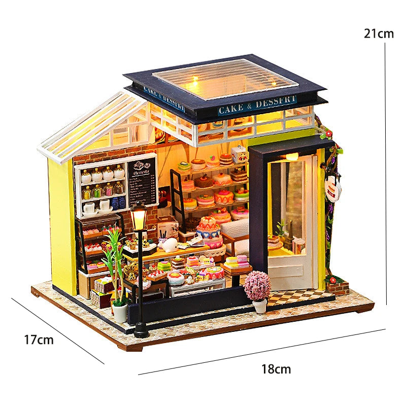 A miniature dollhouse kit featuring a cake and dessert shop with warm lighting and various furniture.