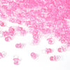 A pile of pink mini acrylic pacifier party favors for baby shower decorations.