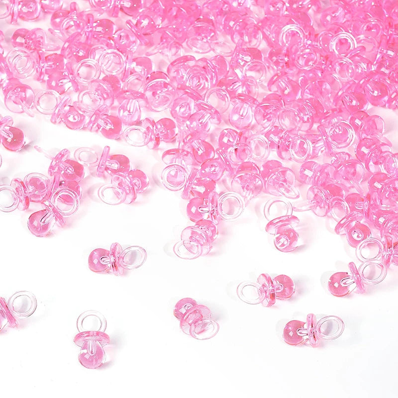 A pile of pink mini acrylic pacifier party favors for baby shower decorations.