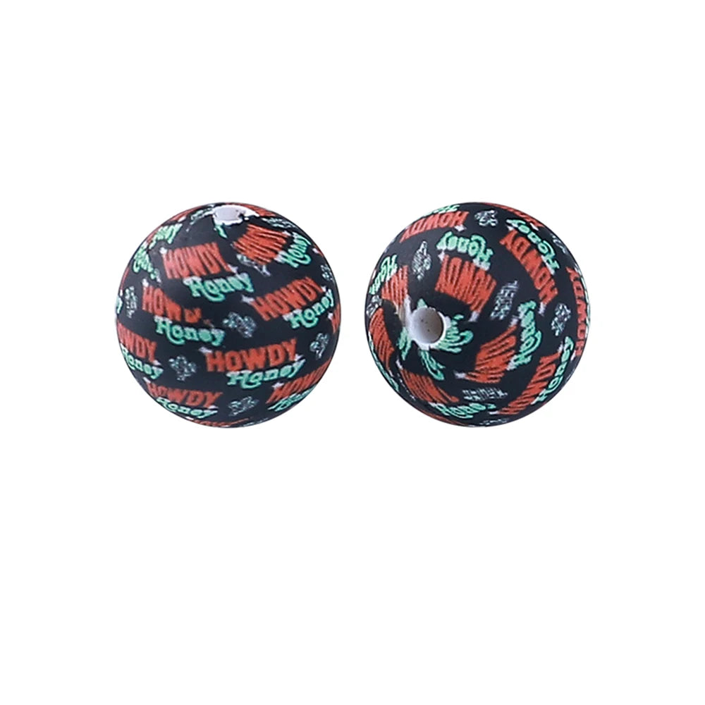A pair of black silicone beads printed with an orange and white pattern featuring the words Honey and Howdy