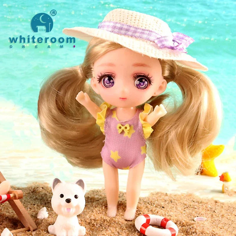 A small doll with long blonde hair wearing a purple outfit and a straw hat standing on a sandy beach.