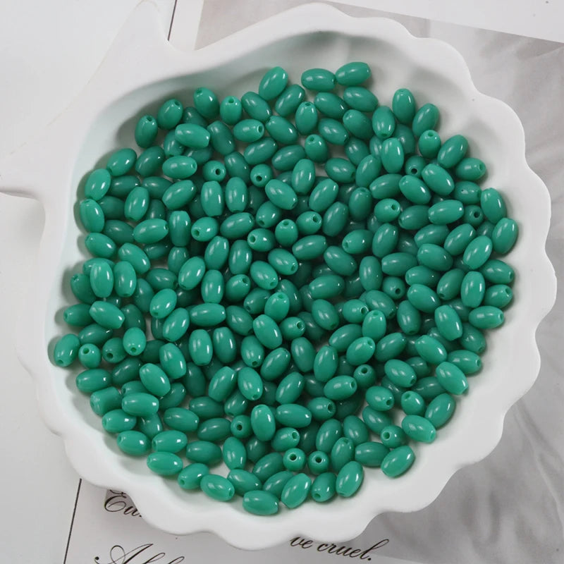 A pile of small, oval, seafoam green glass rice grain beads for jewelry making in a white dish.