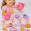 A young girl is holding a pink teapot and pouring tea into cups, surrounded by various colorful pretend play food items.