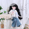 A black-haired doll dressed in a white blouse and blue pants with a lace veil and a small accessory.