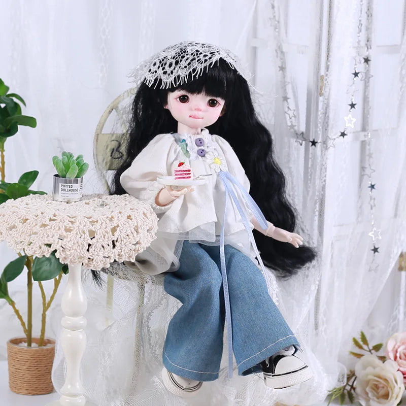 A black-haired doll dressed in a white blouse and blue pants with a lace veil and a small accessory.