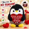 A handmade crochet penguin doll with a red heart and yellow feet, surrounded by red hearts.