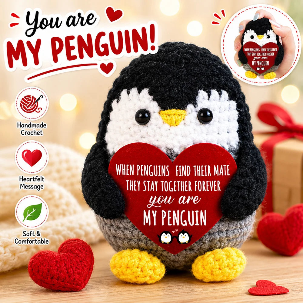 A handmade crochet penguin doll with a red heart and yellow feet, surrounded by red hearts.