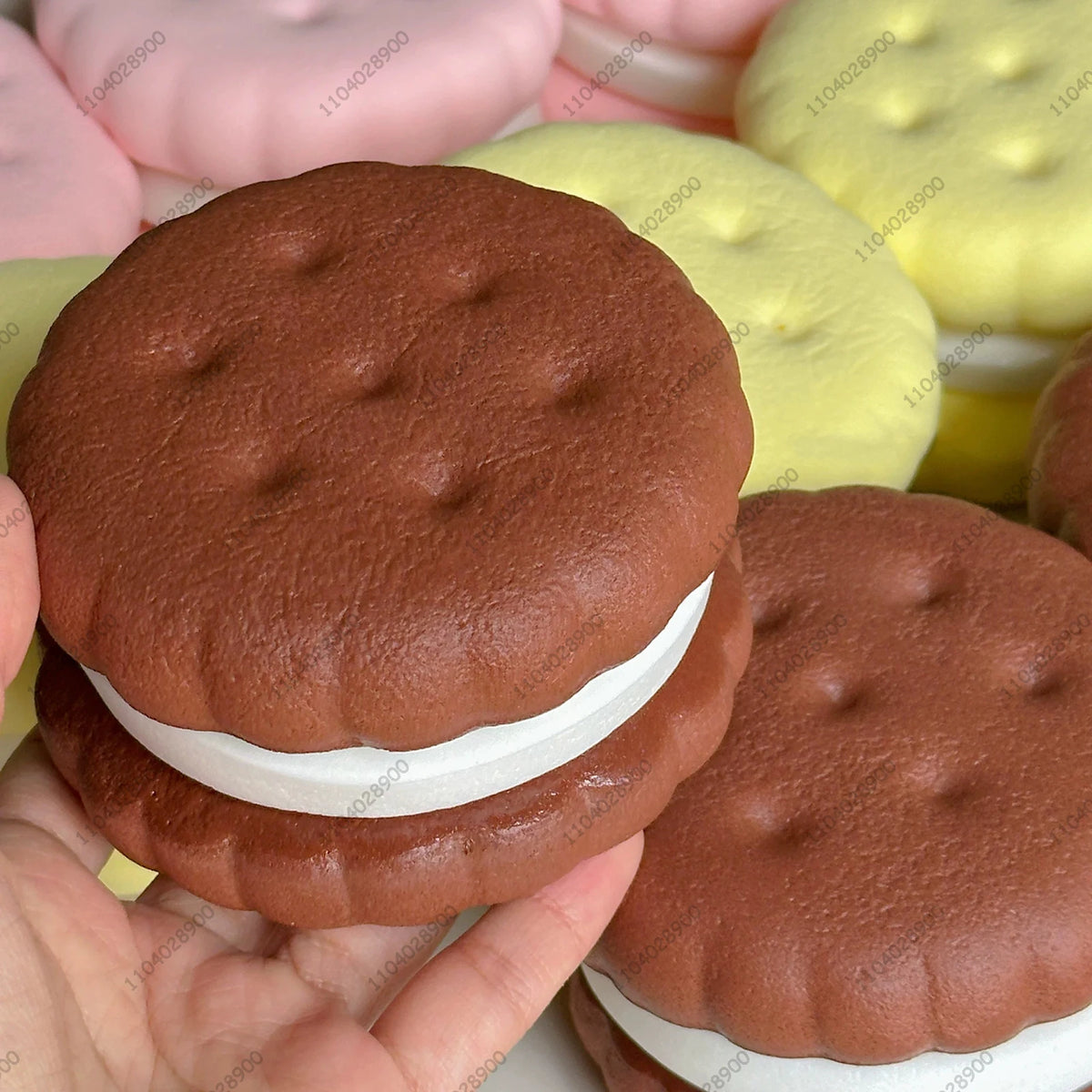 A realistic cake squishy fidget toy in brown and white colors is shown against a background of other squishies.
