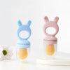 A pink silicone fruit food feeder and cooling mold set with a pink elephant-shaped silicone tool and clear container.