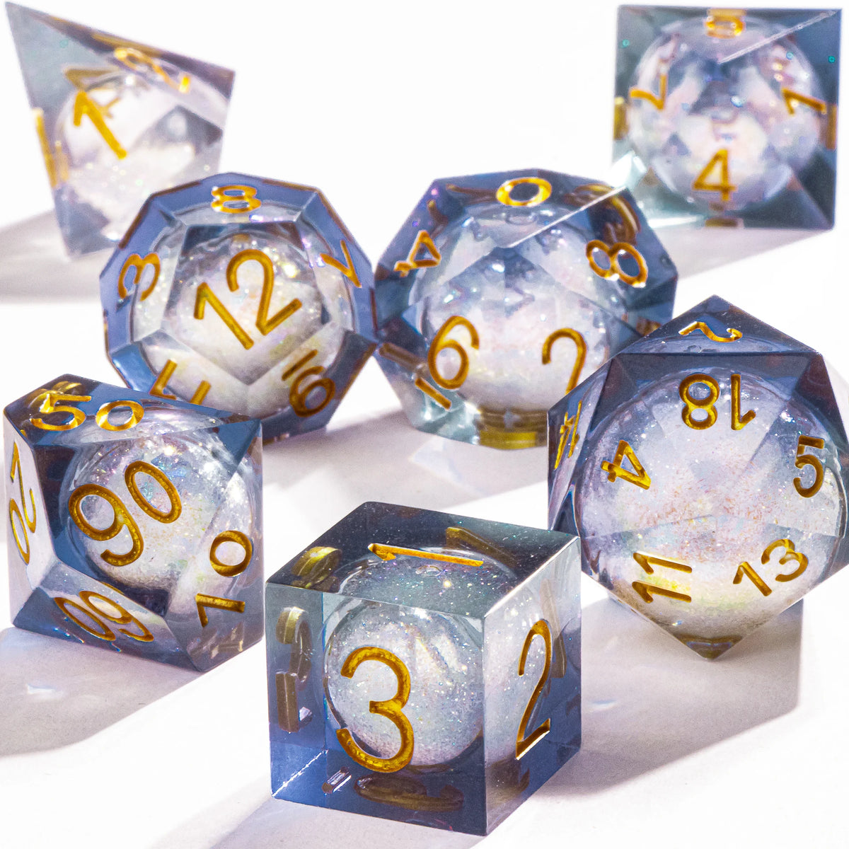 A collection of blue liquid core polyhedral dice with a galaxy finish scattered on a white surface.