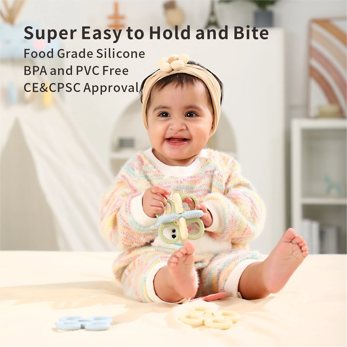 A baby is holding a silicone teether set for babies with various chew toys on a table.