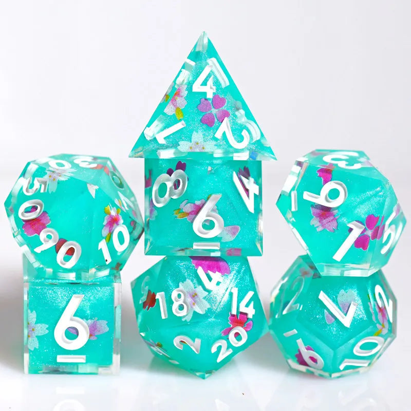 A set of handmade resin polyhedral dice featuring a teal color and pink floral designs.