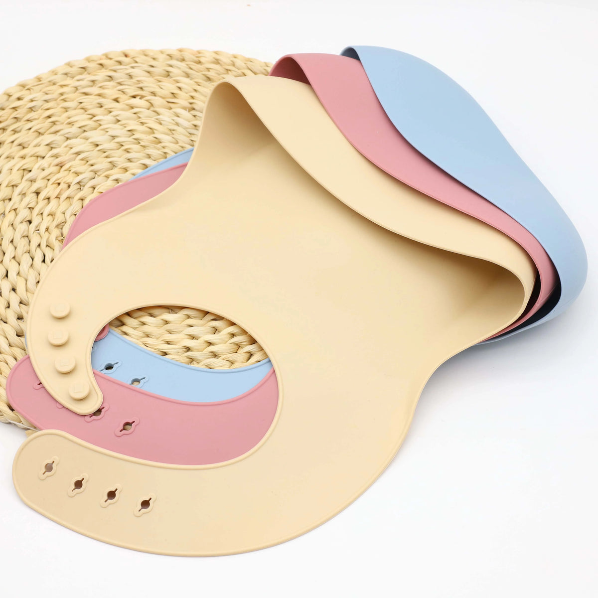 A stack of nine silicone baby tableware pieces in pastel colors, including pink, blue, and beige.