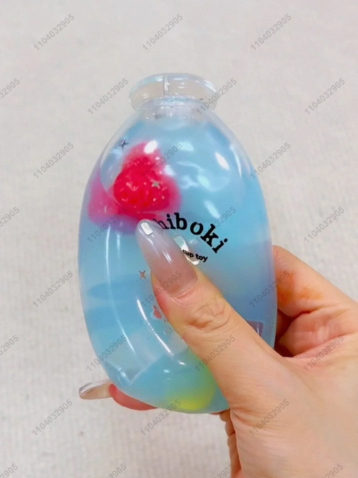 A hand holds a clear blue squishy fidget toy bottle with a pink fruit design.