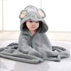 A baby wearing a gray elephant hooded towel, lying on a white surface.