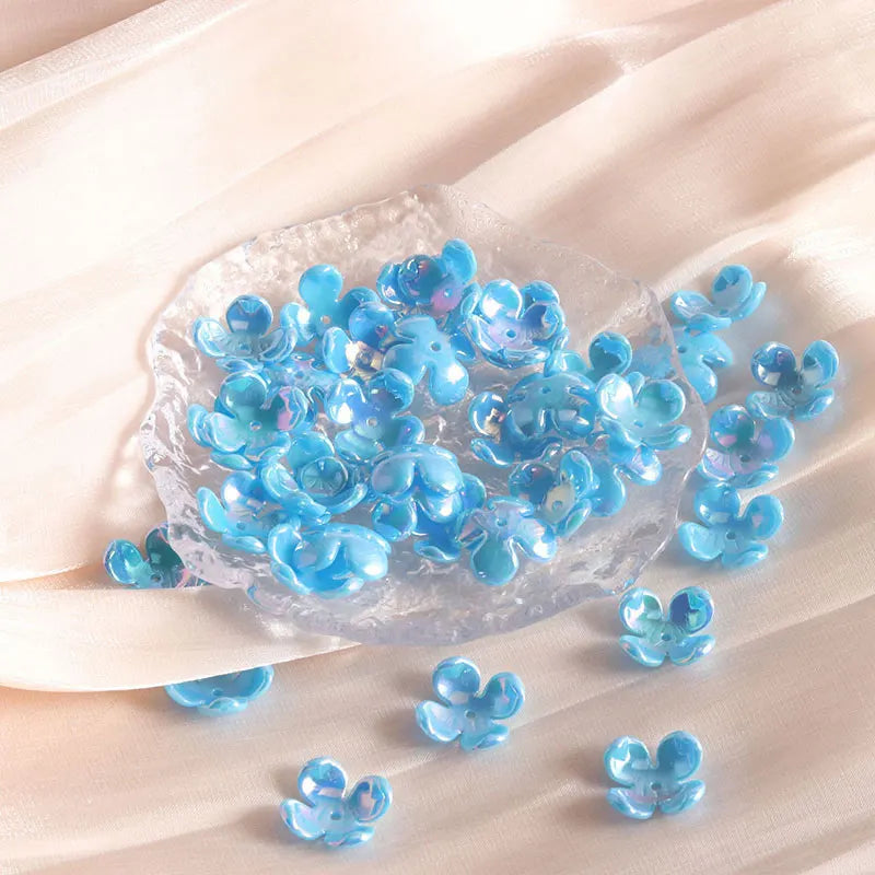 A pile of small, translucent blue acrylic four-petal flower beads scattered on a light fabric.