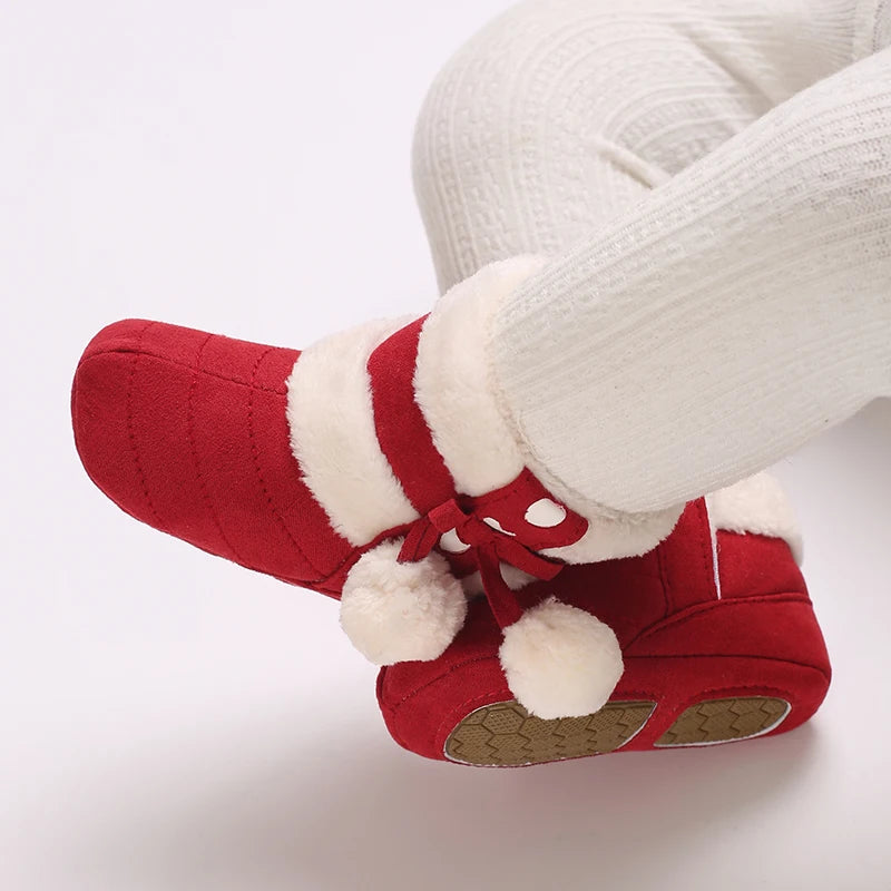 A close-up of a pair of red baby winter boots with white faux fur trim, shown on a person's foot.
