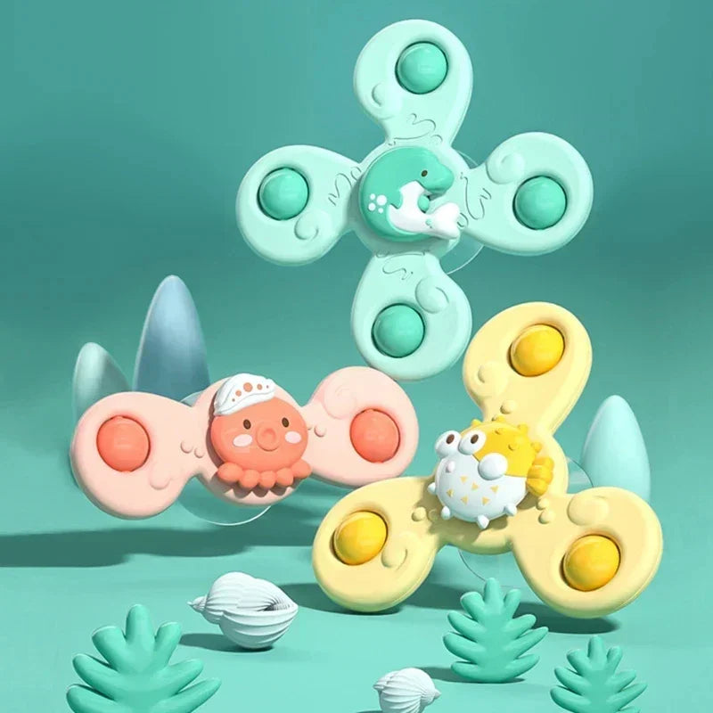 A set of three light green and yellow baby bath toys with suction cup spinners floating in a teal background.