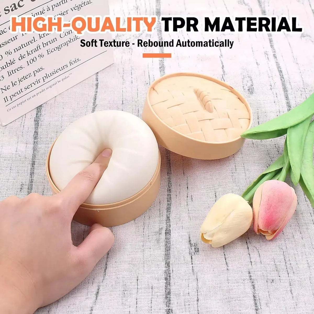 A hand is squeezing a round, beige dumpling squishy stress ball next to a pink and yellow flower.