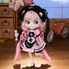 A pink and black fashion doll with long hair and a bow is standing on a wooden floor.