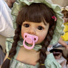 A realistic silicone vinyl toddler doll named Betty with dark hair styled in braids wearing a light green dress.