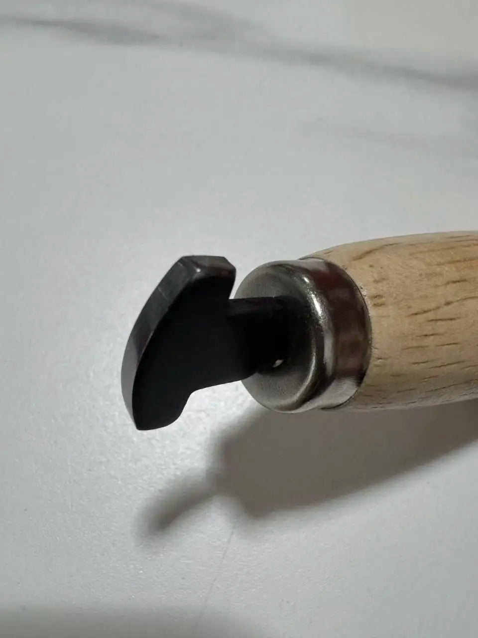 A close-up view of a professional bezel setting pusher tool with a dark metal tip and a light wooden handle.
