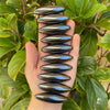 A hand holds a series of smooth, black magnetic olive snake eggs used as a fidget toy against a green leafy background.