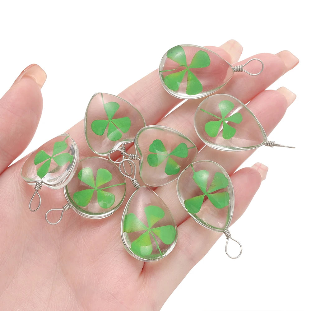 A hand holds a set of handmade glass four leaf clover pendants for jewelry making