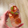 A hand holds a clear bottle filled with orange fruit pieces and a green leaf, labeled Chiboki.