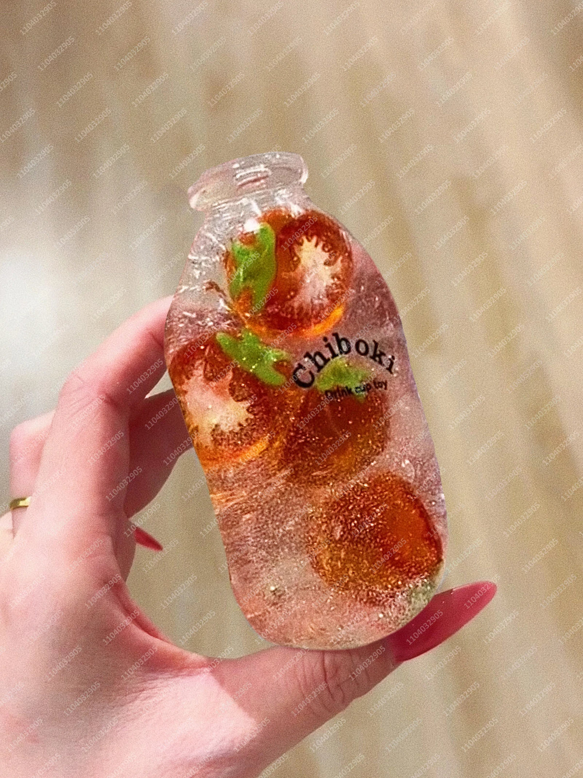 A hand holds a clear bottle filled with orange fruit pieces and a green leaf, labeled Chiboki.
