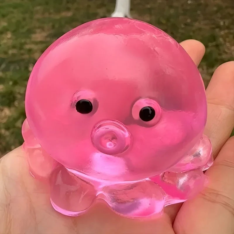 A hand holds a pink squishy ocean octopus fidget toy with large eyes and fins.