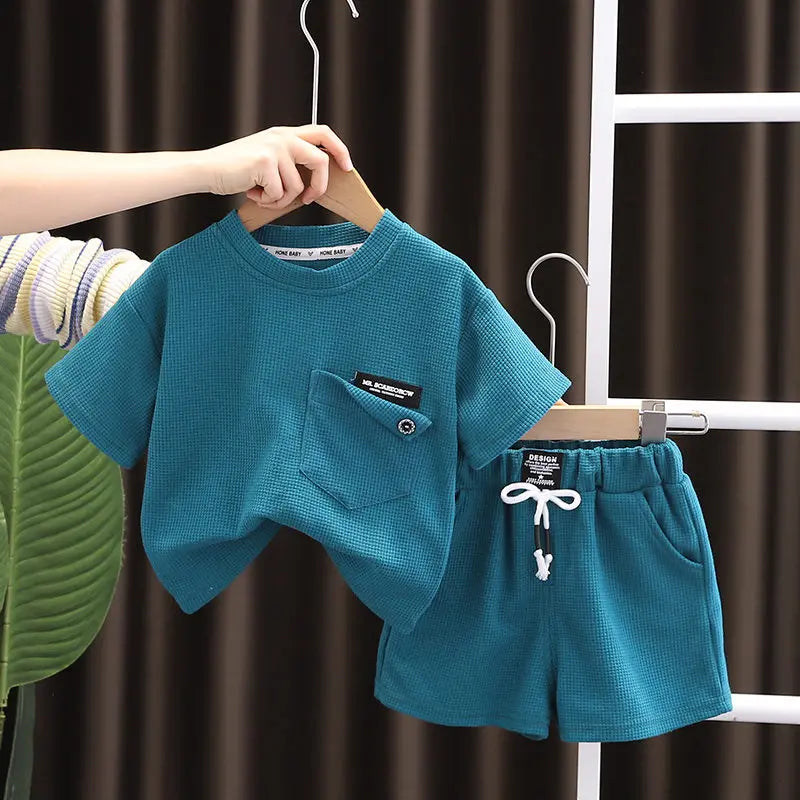 A teal boys' summer cotton t-shirt and shorts set being hung on a white hanger.