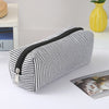 A striped canvas pencil case with a black zipper is shown lying on a white surface.
