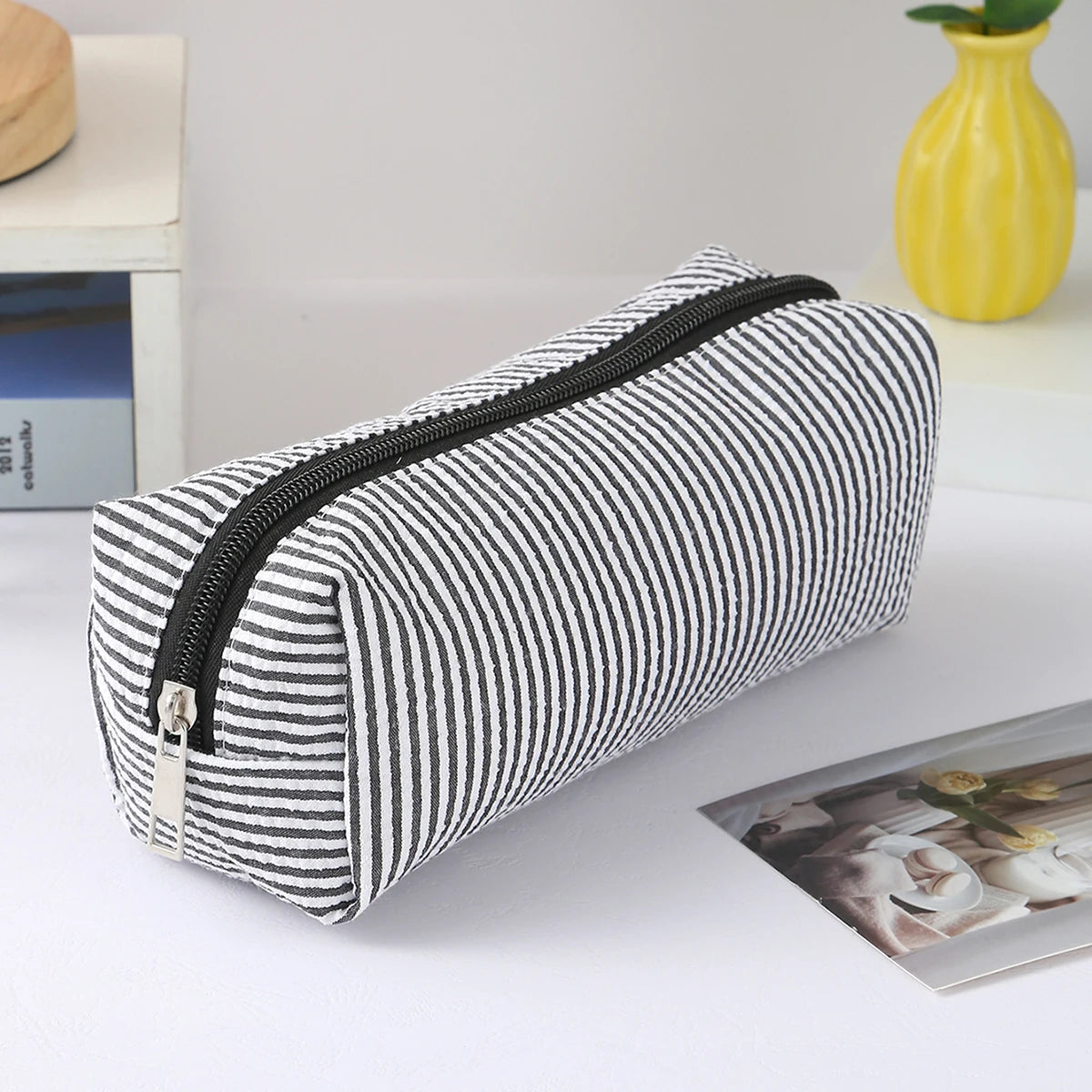A striped canvas pencil case with a black zipper is shown lying on a white surface.