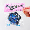 A clear plastic bag contains a dark blue cat paw squishy fidget toy and small blue glitter pieces.