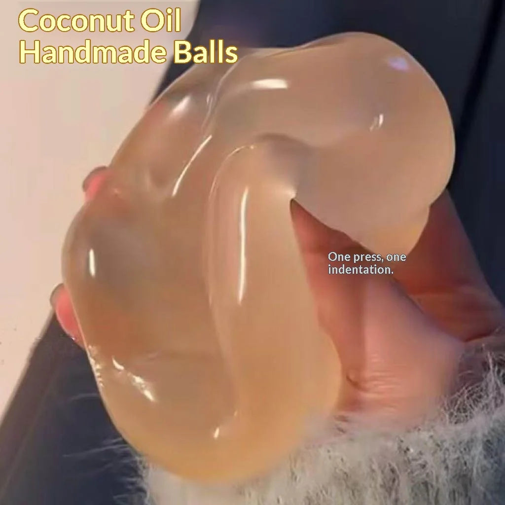 A hand holds a translucent, pale orange coconut oil handmade ball with an indentation.