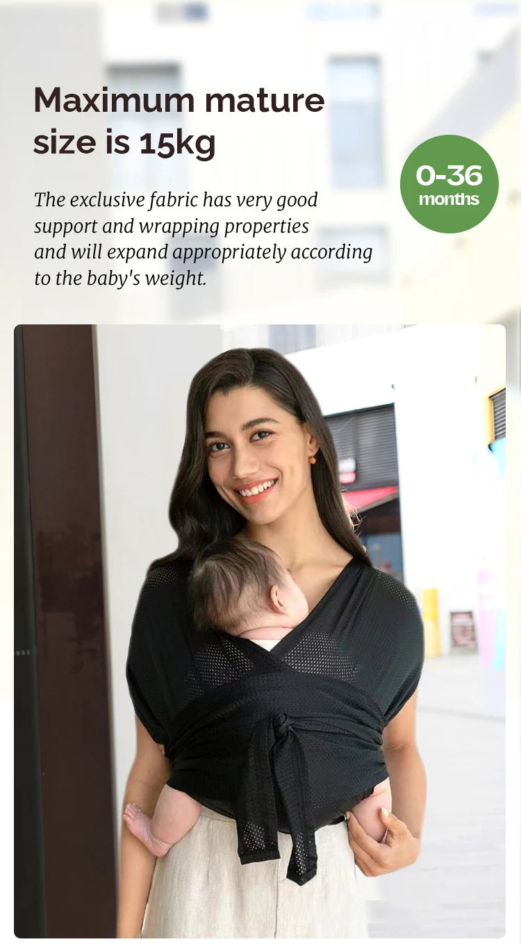 A woman is holding a baby in a black X-shaped baby sling carrier.