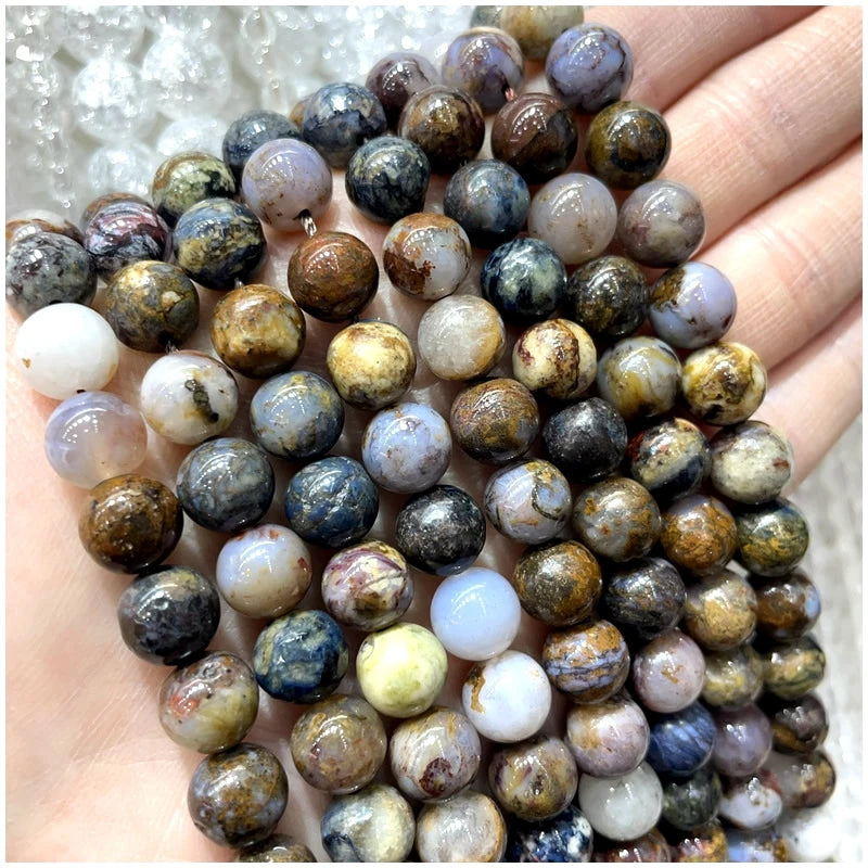 A hand holds a string of natural stone beads including amethyst, garnet, and labradorite for jewelry making