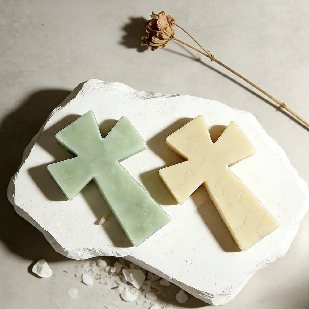 Two pale green and yellow silicone cross molds resting on a white stone with a dried flower stem.