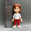 A figurine of a girl with reddish hair wearing a white shirt and red pants, standing next to a ruler.